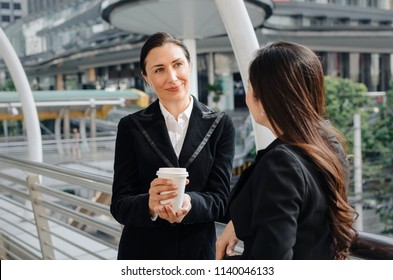two business asian and caucasian woman with coffee cup talking about finance news together in the modern city, congratulation, success, meeting, partner, teamwork, community and connection concept