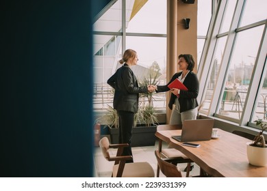 Two business colleagues handshaking while standing at the office - Powered by Shutterstock