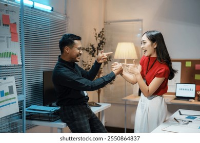 Two business colleagues are playfully pointing at each other and laughing during a late night at the office - Powered by Shutterstock