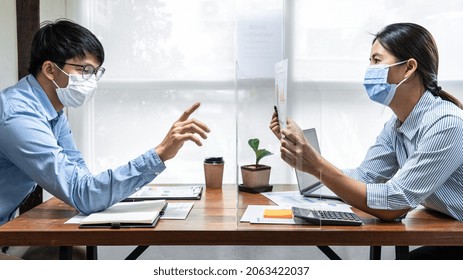 Two business colleagues showing and pointing on financial document for discussion in new business while wearing face mask and working together with table shield partition to keep social distancing - Powered by Shutterstock