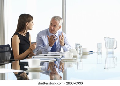 Two Business Colleagues Sitting Around Boardroom Table Having Informal Discussion