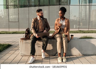 Two Business Colleagues Sitting On Bench And Talking To Each Other Outdoors