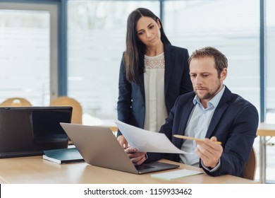 Two Business Colleagues Working On A Document Together At A Desk In The Office Proof Reading The Contents Or Brainstorming A Problem