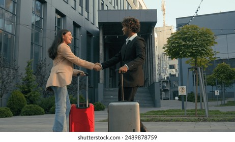 Two business coworkers people Arabian businesswoman meeting in city airport terminal handshaking Indian businessman with luggage baggage trip woman man travel meet handshake greeting shaking hands - Powered by Shutterstock