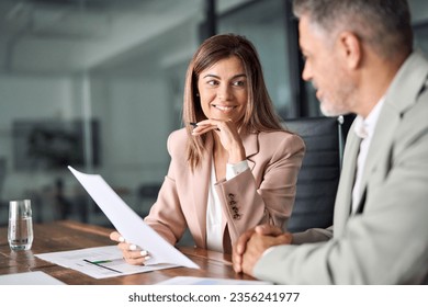 Two business executives discussing financial legal papers in office at meeting. Smiling female lawyer adviser consulting mid aged client at meeting. Mature colleagues doing project paperwork overview.