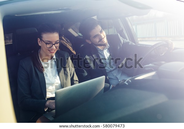 Two business friends in the car.They\
travel to business meeting.Man drives a car while female using\
laptop and preparing for presentation.\
