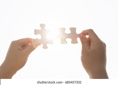 Two business man hands connecting two white jigsaw puzzle pieces with beautiful sun sky background. Business concept. Cooperation and success concept. Teamwork. - Shutterstock ID 685457332