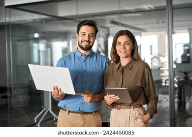 Two business partners executives standing in office looking at camera. 2 sales managers, company agents, consultancy professionals, bank advisors with devices posing for corporate portrait.