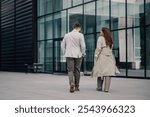 Two business partners walking and talking outside the office building during a work break, exuding confidence and professionalism in elegant suits against a modern city backdrop