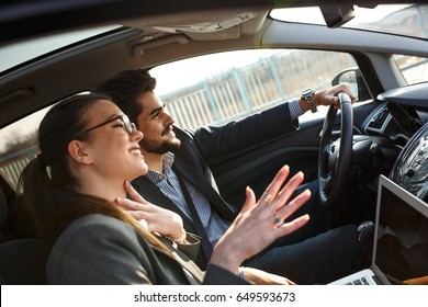 Two Business People In The Car.They Travel To Business Meeting.Man Drives A Car While Female Using Laptop And Preparing For Presentation.