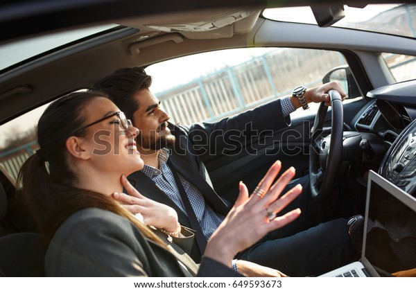 Two business people in the car.They travel\
to business meeting.Man drives a car while female using laptop and\
preparing for presentation.