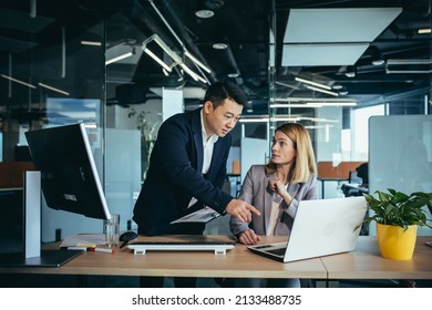 Two Business People Consulting On A Project Looking At Computer Monitor Screen Sitting In The Office. Asian Male Employee Coworker Explains Colleagues Ideas And Strategies Accountant, Financial Report