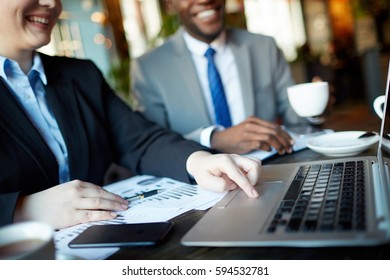 Two business people during work meeting in modern cafe: Closeup shot female hands using laptop touchpad while discussing business with smiling partner over documents with charts and graphs - Powered by Shutterstock