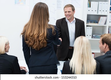 Two Business People, A Man And Woman, Shaking Hands Across A Table In A Meeting Sealing An Agreement Or Business Deal