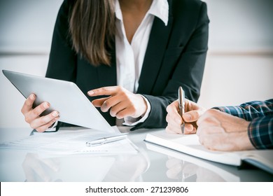 Two Business People In A Meeting Discussing Information On A Tablet-pc And Taking Notes As They Work Together As A Team, Close Up View Of Their Hands Seated At A Desk