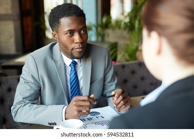 Two Business People Meeting In Modern Cafe: African-American Man Wearing Business Suit Looking At His Partner Listening Intently