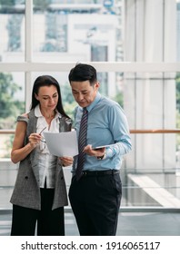 Two Business People Reading Papers Together In Modern Office With Big Windows.
Two Serious Business People Standing And Talking About Documents In Office Lobby