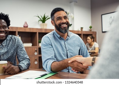 Two business people shaking hands while sitting in meeting room. Middle eastern businessman shake hands to businesswoman. Portrait of happy smiling latin man signing off deal with an handshake.