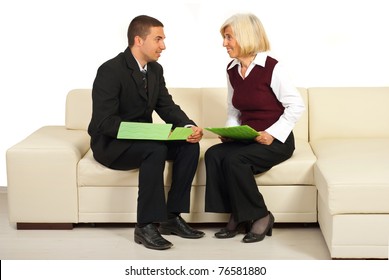 Two Business People Sitting On Sofa In Office Holding Folders And Having Happy Conversation