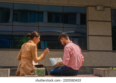 Two Business People Are Sitting And Working Outside In The City, Happy, On A Beautiful Sunny Day