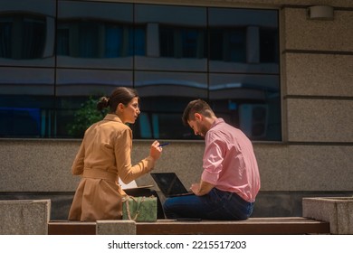 Two Business People Are Sitting And Working Outside In The City, Happy, On A Beautiful Sunny Day