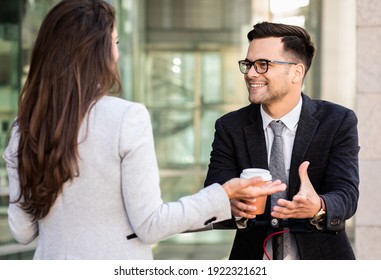 Two Business People Standing Outside In Front Of Modern Business Building.