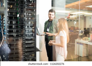 Two business people standing in server room with laptop and discussing