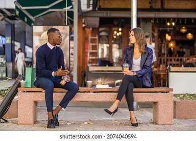 Two business people are talking in front of the cafe while sitting on the bench