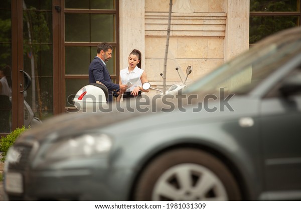 Two business people are talking in front of\
the company while the car is\
crossing