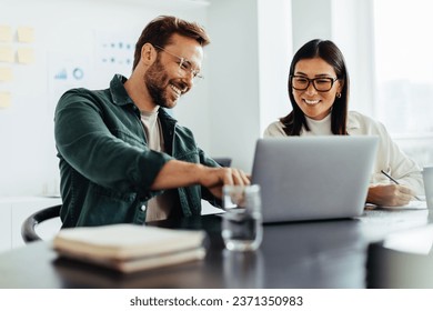 Two business people using a laptop together while sitting in a meeting. Happy business people looking at a slide presentation in an office.