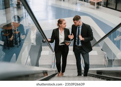 Two business people using tablet computer while going up the escalator. - Powered by Shutterstock