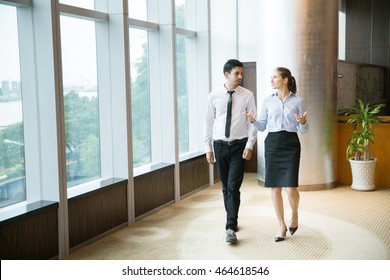 Two Business People Walking In Office And Talking To Each Other