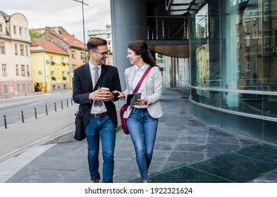 Two Business People Walking Outside In Front Of Modern Business Building.