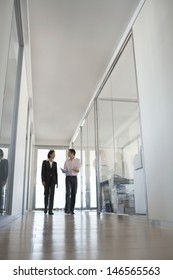 Two Business People Walking While Talking In Hallway