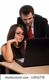 Two Business People Wearing Black Business Attire Brunette Woman With Eyeglasses And Man With Red Tie Woman Sitting At Desk In Front Of Computer With Man Leaning Over Both Looking At Screen