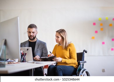 Two Business People With Wheelchair In The Office.