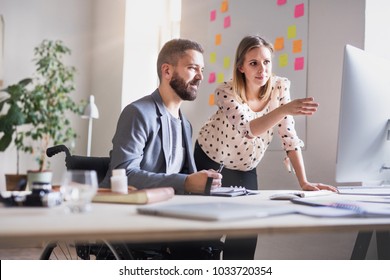 Two Business People With Wheelchair In The Office.