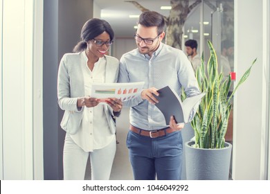 Two Business People Working Together With Documents While Having Informal Meeting In Office Hallway.