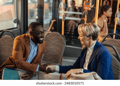 Two business people, a young black man and a middle-aged white woman, greeting each other on a public bus with a handshake. - Powered by Shutterstock