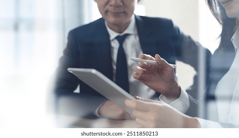 Two business person using digital tablet and having a discussion in office. Asian business team, colleague working together. Partnership, Teamwork and collaboration, corporate business, close up - Powered by Shutterstock