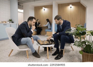 Two business professional men playing chess in office cafe, sitting at board, moving pieces, enjoying break, smart game, hobby, leisure time, entertainment, training intelligence, strategic skills - Powered by Shutterstock