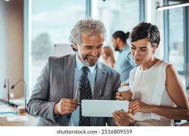 Two business professionals engaging in a lively discussion over a tablet in a bright office environment. The scene conveys teamwork, collaboration, and modern workplace dynamics. - Powered by Shutterstock