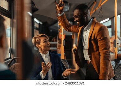 Two business professionals having a conversation on a bus. One is seated and the other is standing, holding onto a handrail. - Powered by Shutterstock