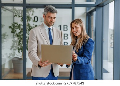 Two business professionals with a shared expression of joy working together, brainstorming ideas, and discussing content on a laptop in a modern corporate environment