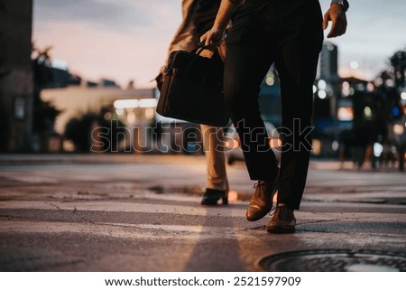 Two business professionals walking on a city street at night, one carrying a briefcase. The scene highlights night business, professionalism, and urban lifestyle.
