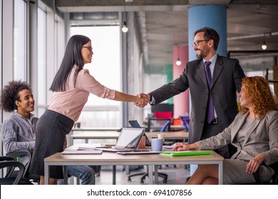 Two business teams successfully negotiating, shaking hands. At meeting table business groups shaking hands on completed deal. Man and woman handshake. - Shutterstock ID 694107856
