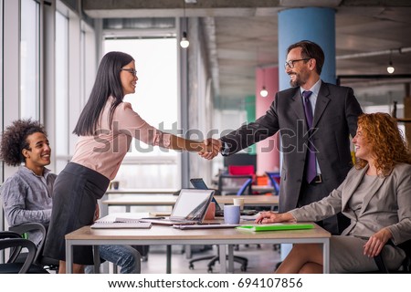 Two business teams successfully negotiating, shaking hands. At meeting table business groups shaking hands on completed deal. Man and woman handshake.