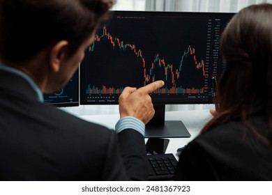 Two business traders discussing on dynamic stock market in currency rate investment trading on two pc screens with compare real time graph on risk or profit point of data at modern office. Postulate. - Powered by Shutterstock