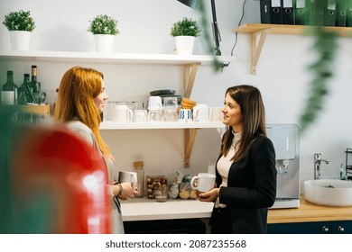 Two business woman drinking coffee, in a white mug, during a break at the coffee area in the office - Powered by Shutterstock