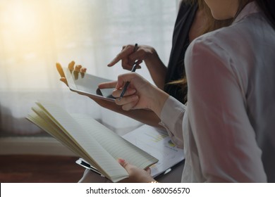 Two Business Woman In A Meeting Discussing Information On A Tablet And Taking Notes As They Work Together As A Team,